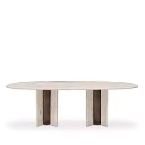 The Paris Oval Dining Table showcases a smooth, oval travertine marble top supported by two striking, textured marble bases.