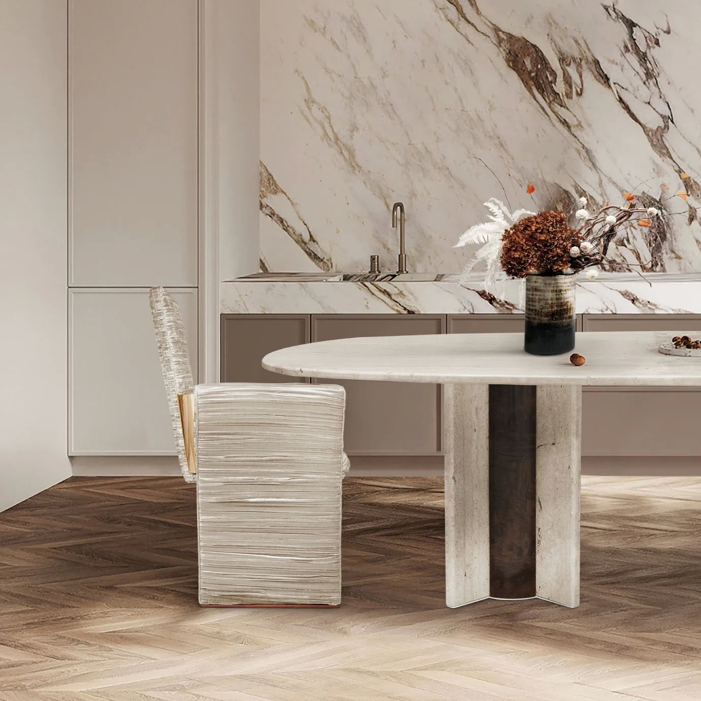 Close-up of the Paris Travertine Marble Oval Dining Table by KOKET with upholstered designer chair, marble tabletop centerpiece, and herringbone wood flooring in a modern luxury dining room.