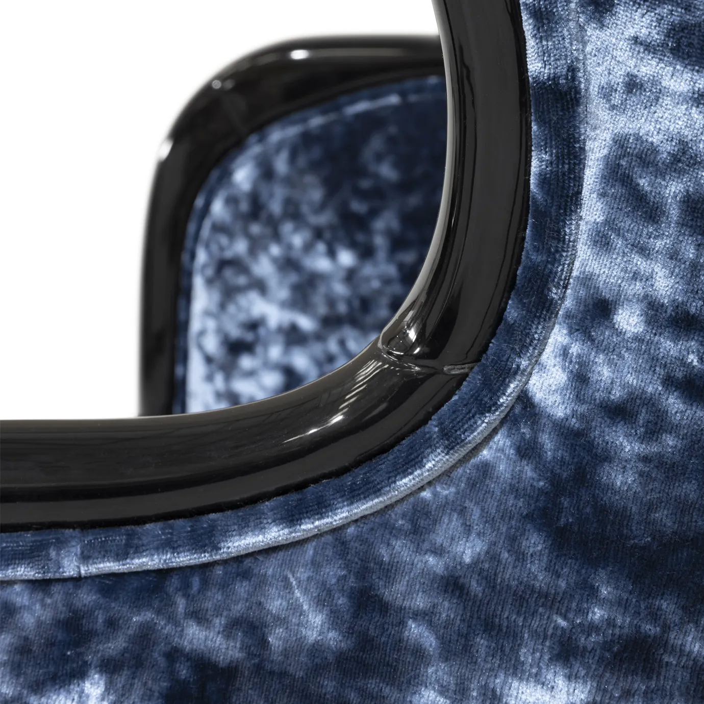 Close-up on the Nudesse Chair's armrest, showcasing its curved, black lacquered frame that contrasts with the plush blue velvet.