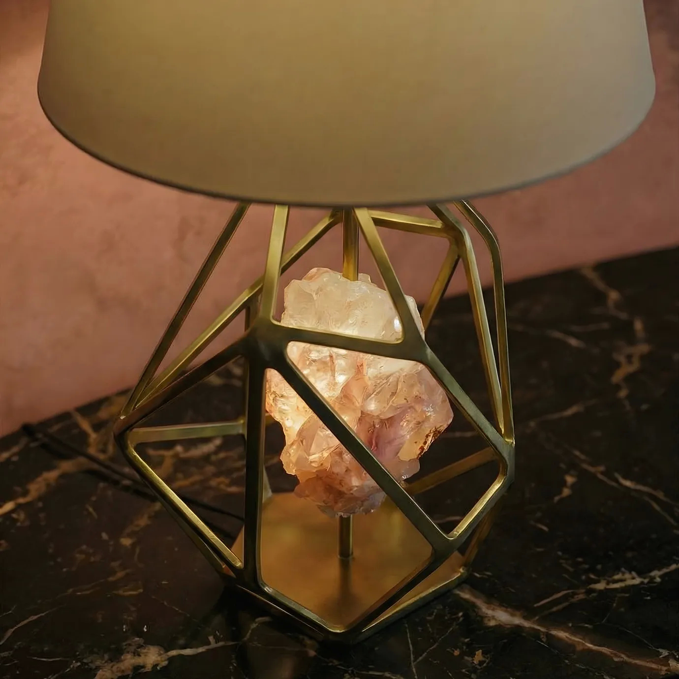 Close-up of the KOKET Gem Table Lamp featuring a sculptural geometric brass frame and a raw crystal core, styled on a dark marble surface for a luxurious interior design aesthetic.