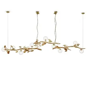 The Hera Suspension Lamp: golden branches with leaves and glass orbs, suspended against a stark white background.