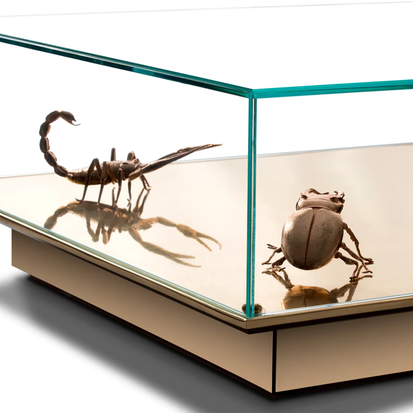 Close-up of golden scorpion and beetle sculptures inside a mirrored glass Metamorphosis table.