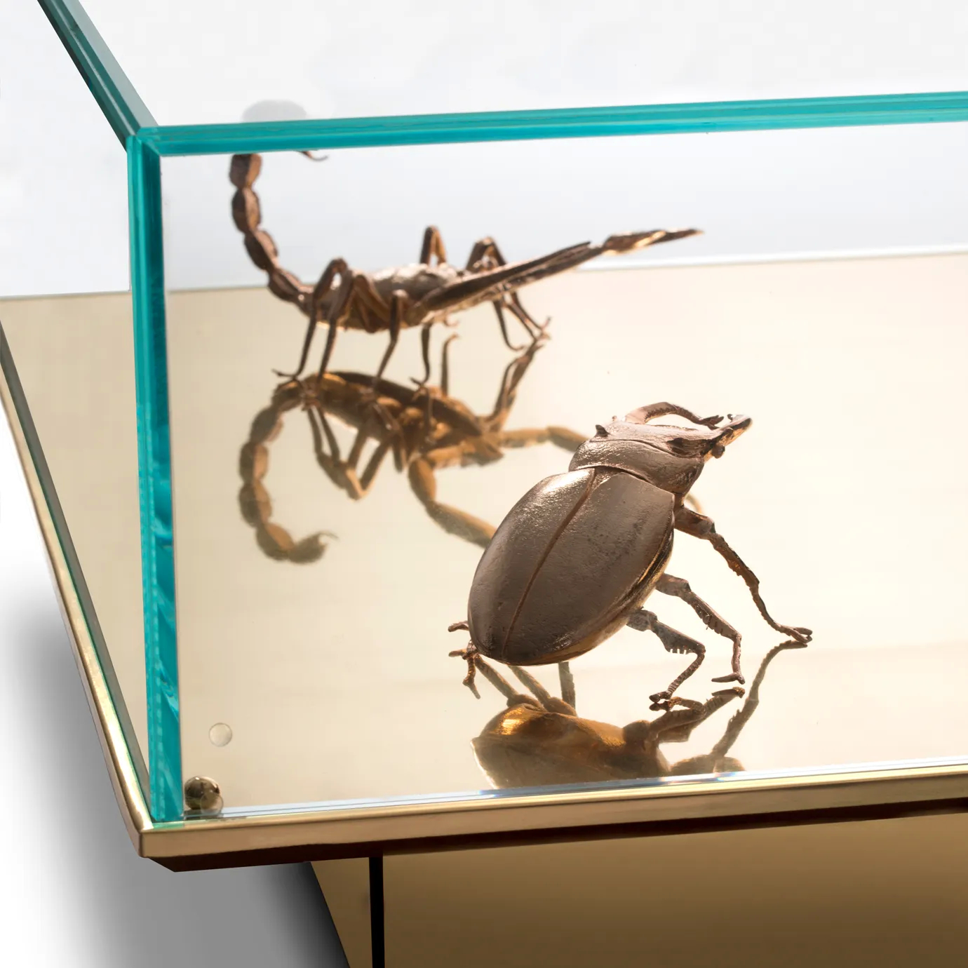 Close-up of golden scorpion and beetle sculptures inside a mirrored glass Metamorphosis table.