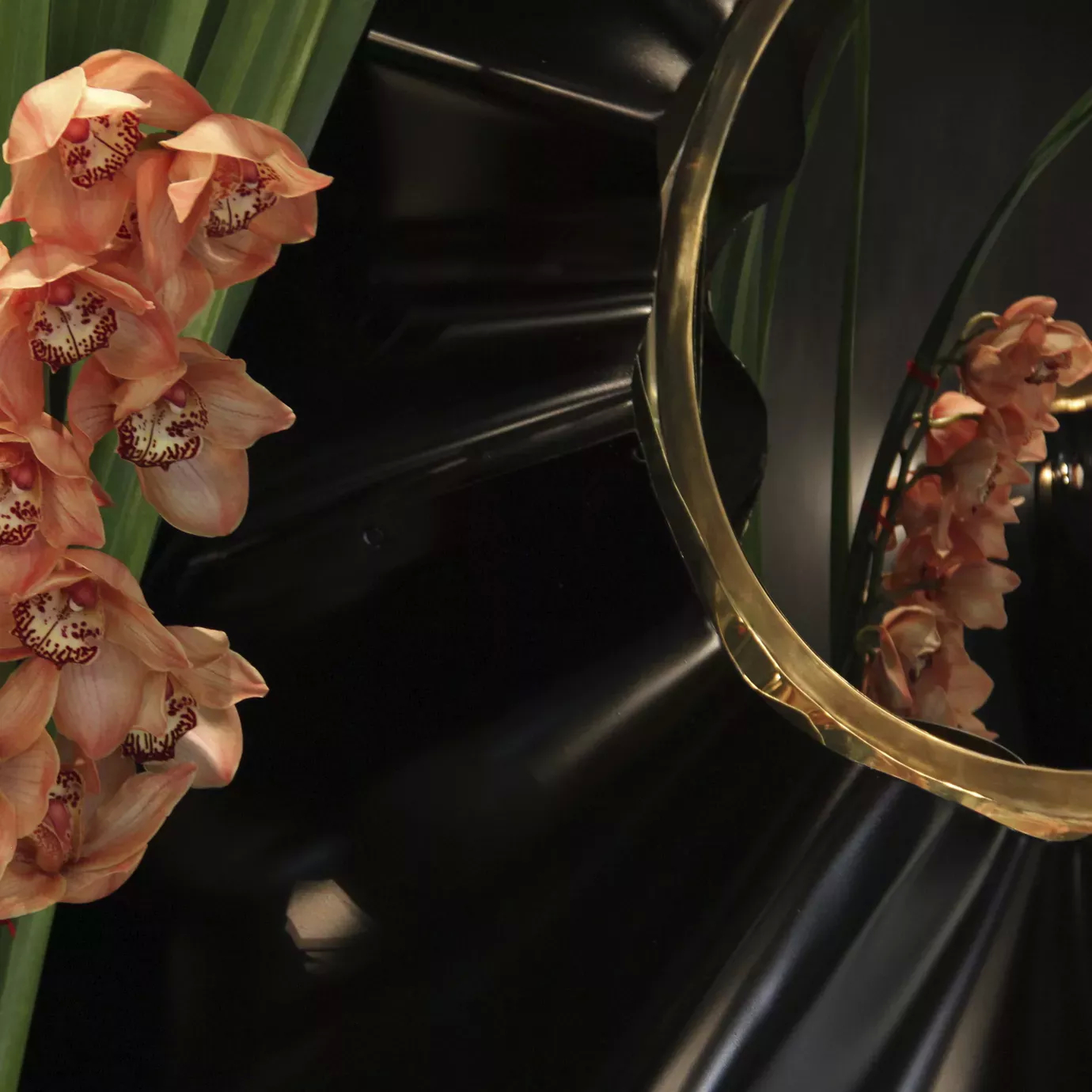 Revê 2 Tier Mirror, with a convex mirror with two rings around it, a black and a golden one, with an orchid by its side.