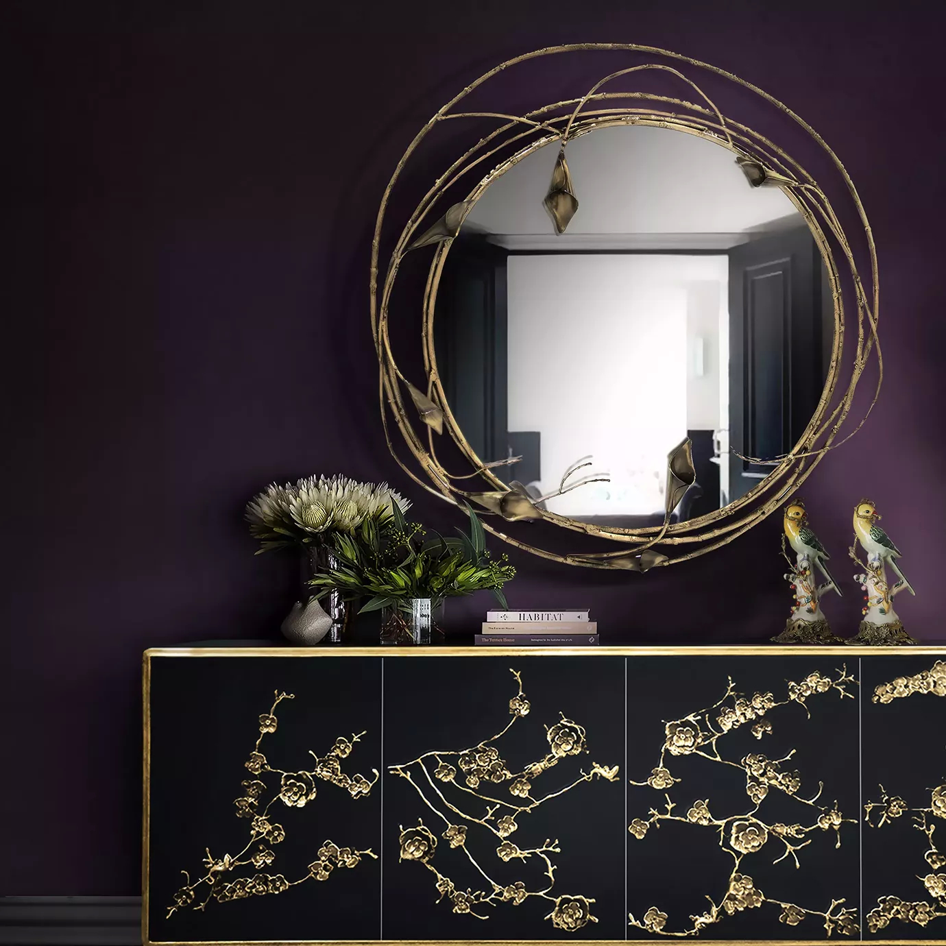 An elegant copper toned Stella Mirror with intricate stem and calla lilies design, accompanied by a black cabinet with golden floral motifs.
