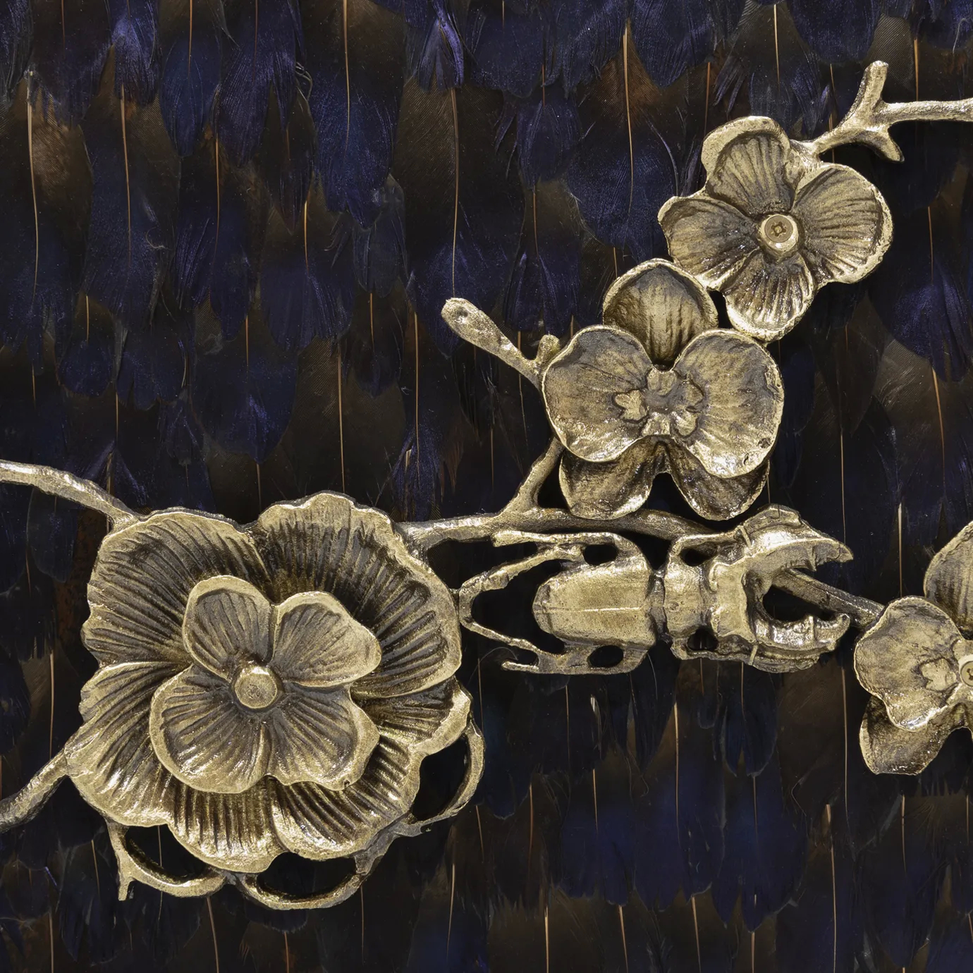 Close look on the golden floral themed ornaments present on the front doors of the Spellbound Purple Feather Cabinet, contrasting with its purple peacock feather adorned structure.