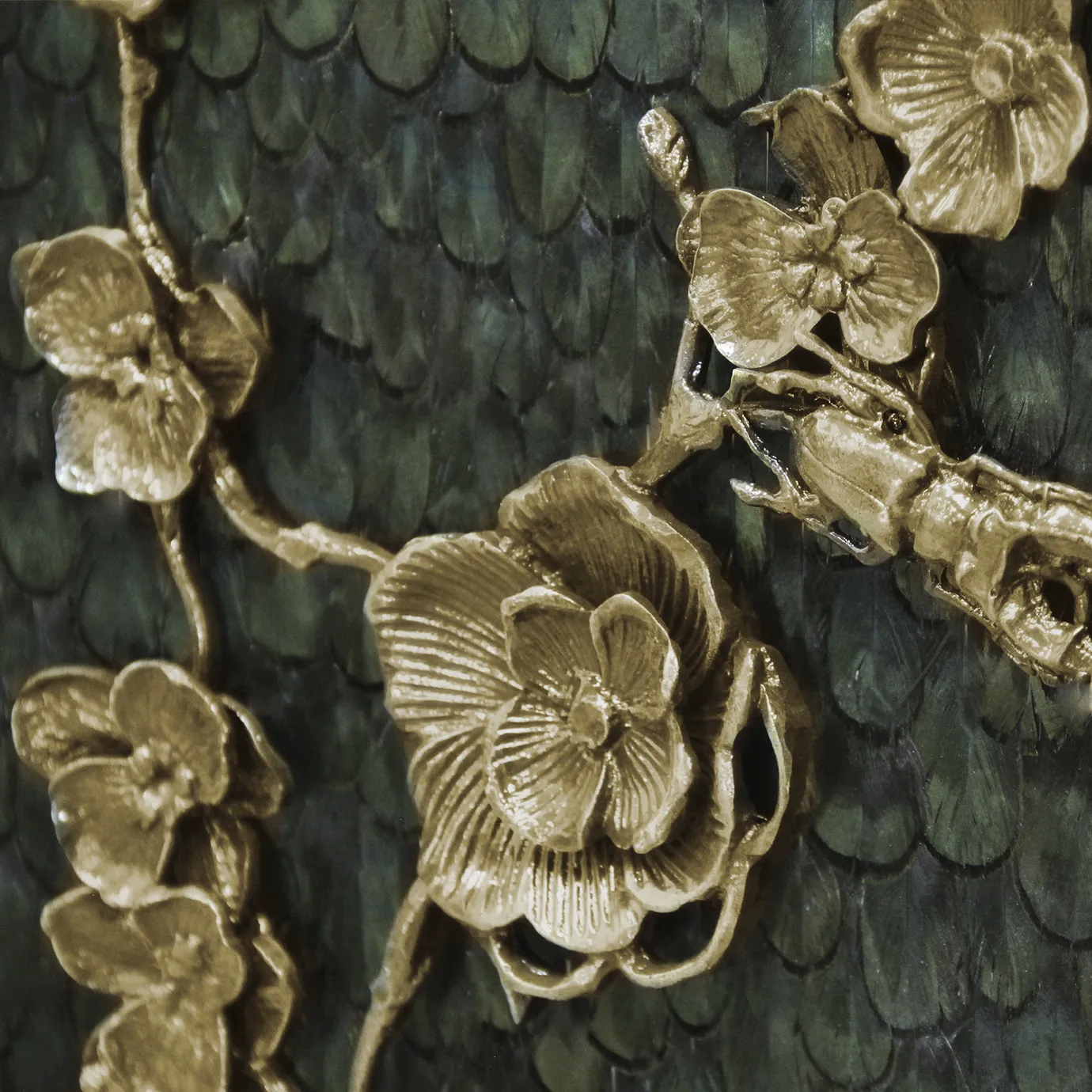 Close look on the golden floral themed ornaments present on the front doors of the Spellbound Peacock Feather Cabinet, contrasting with its greenish peacock feather adorned structure.