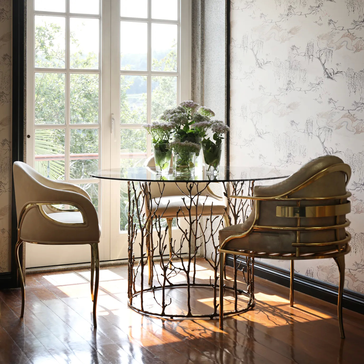The Chandra Dining Chair in cream by KOKET, placed in a stylish interior setting, highlighting its luxurious upholstery, open back design, and polished brass legs.