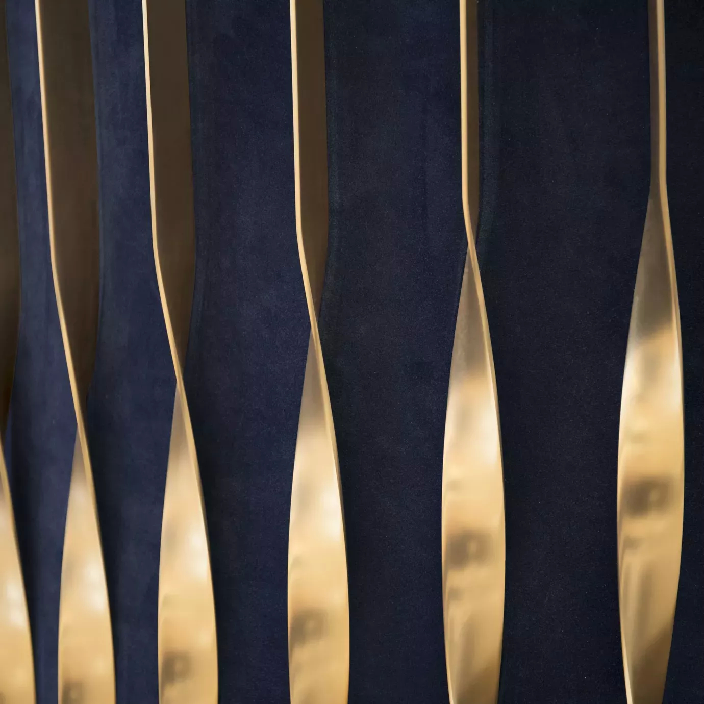 Elegant close-up of the detail of the golden satin brass frame and deep blue velvet upholstery of the Mandy Armchair.