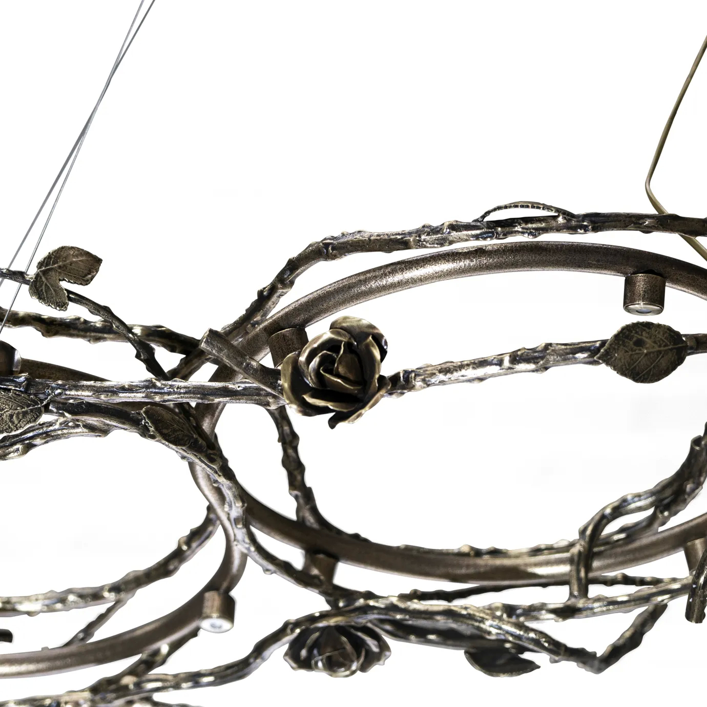Rose Chandelier in aged brass with sculptural vine-like branches and delicate bud details, suspended by thin cables in a modern interior setting.