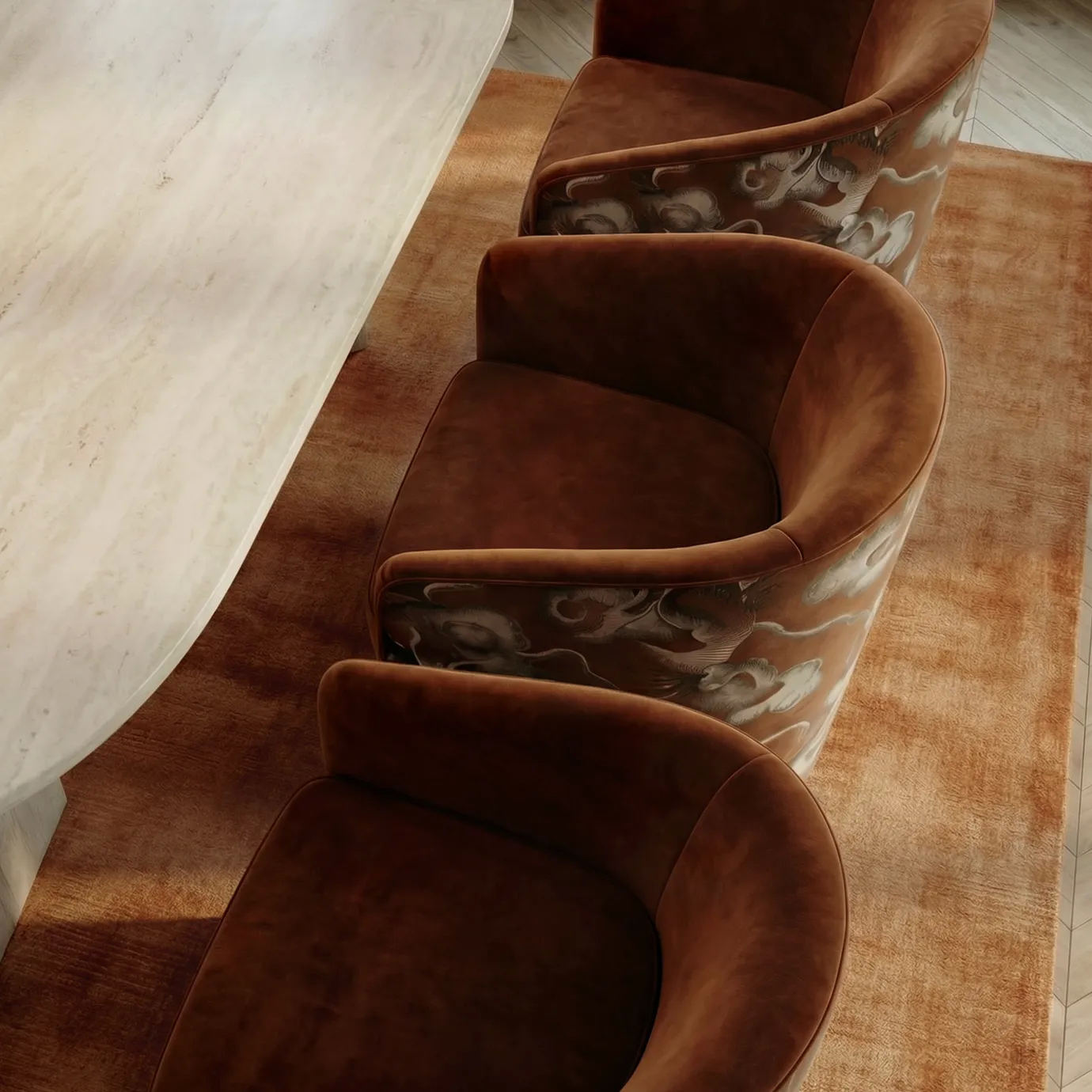 Top-down view of KOKET’s Marseille Chair in rust velvet with swirling embroidery, paired with a travertine table and warm-toned rug—an iconic and sculptural seating piece admired in luxury interiors.
