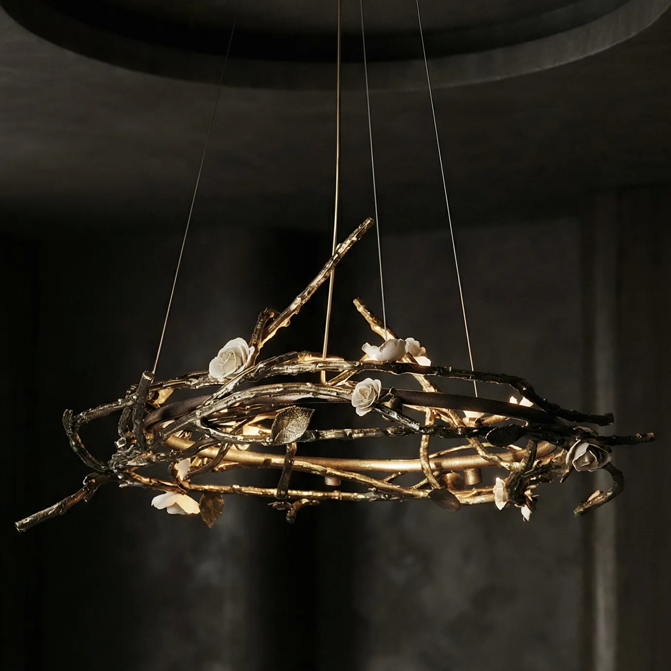 Rose Round Chandelier in aged brass with sculptural branches, metallic leaves, and cream rose-shaped accents, suspended by thin wires in a modern interior.