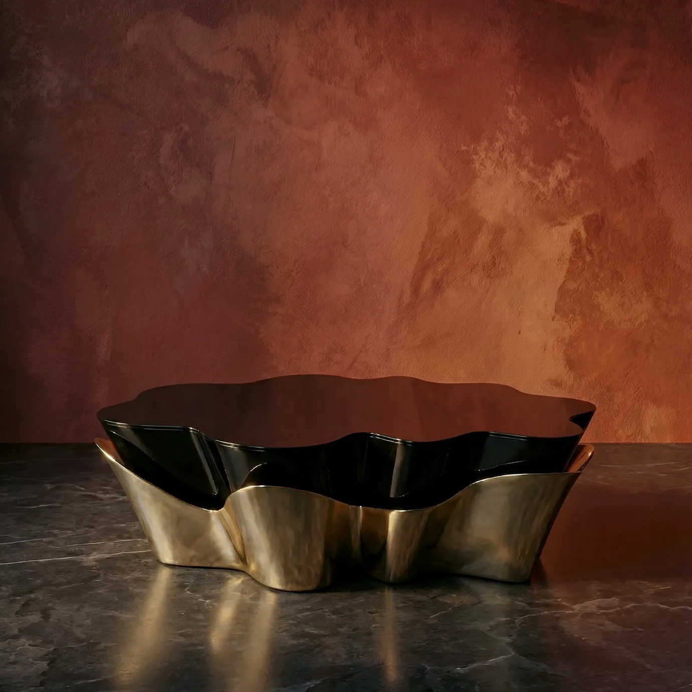 Yasmine Coffee Table by KOKET with sculptural polished brass base and high-gloss black lacquer top, set against a warm terracotta wall, luxury designer coffee table.
