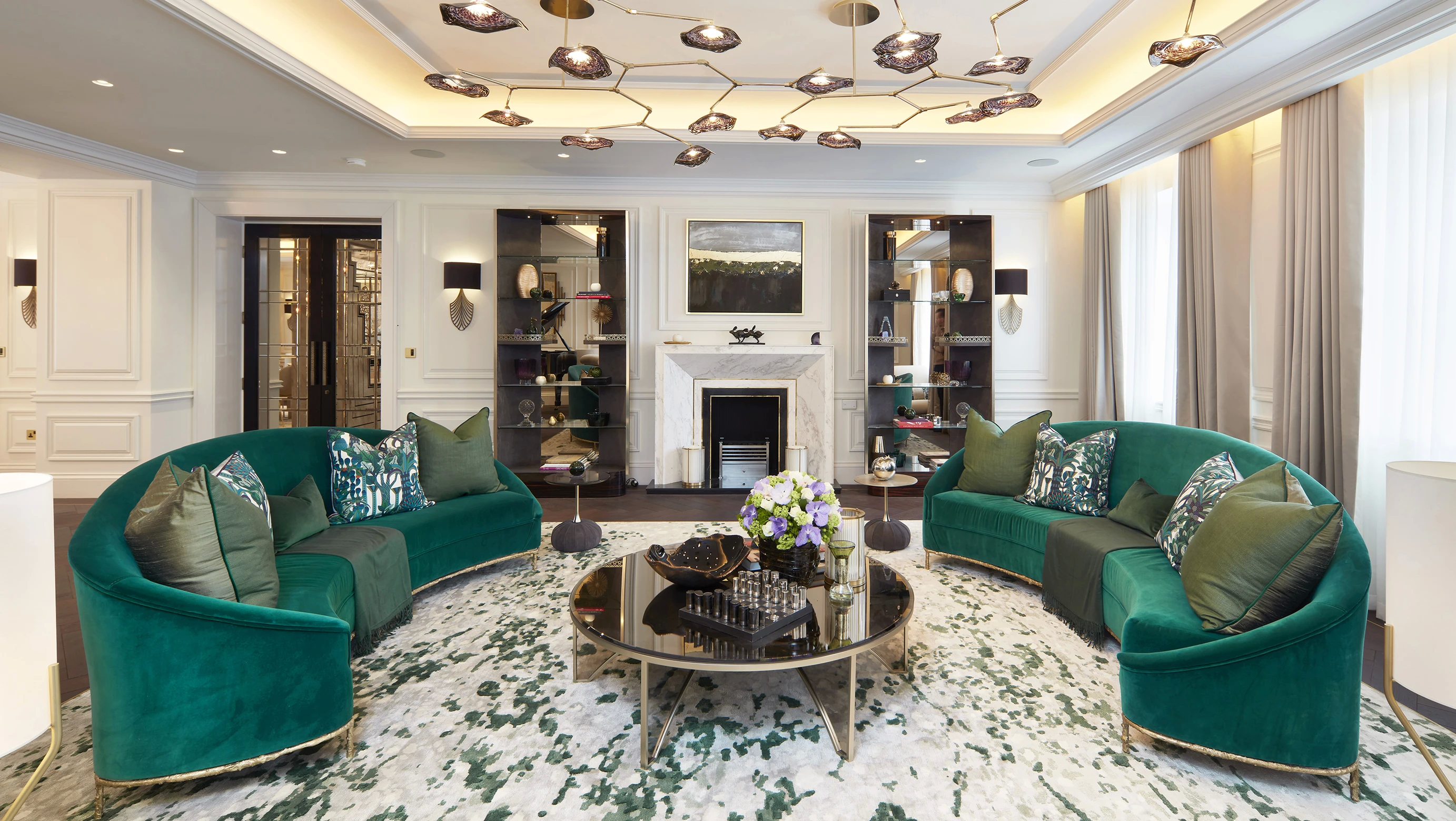Koket's Penthouse Apartment features two emerald velvet sofas, a round coffee table, and a unique branch-like chandelier.