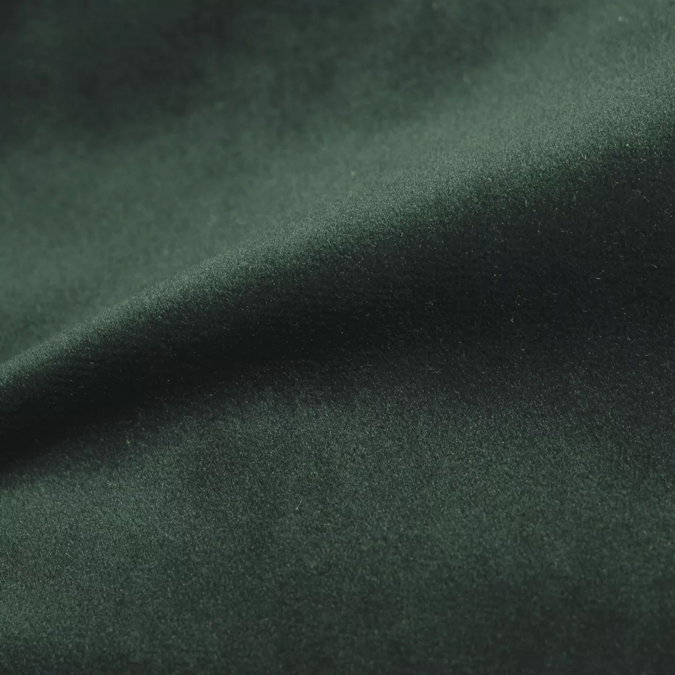 Elegant close-up of a Cozy Velvet Black Forest fabric swatch in a dark and mysterious forest green tone, showcasing its velvety texture and the gentle folds that give it an intense and cozy depth.