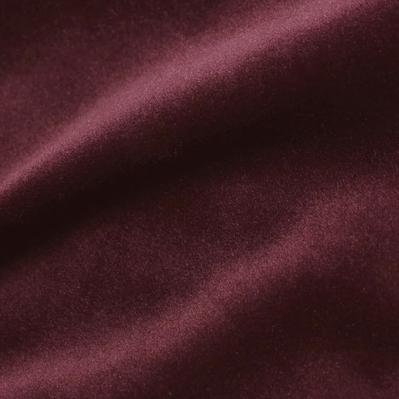 Elegant close-up of a Cozy Velvet Syrah fabric swatch in a deep and sophisticated burgundy tone, showcasing its velvety texture and the gentle folds that highlight its color richness.