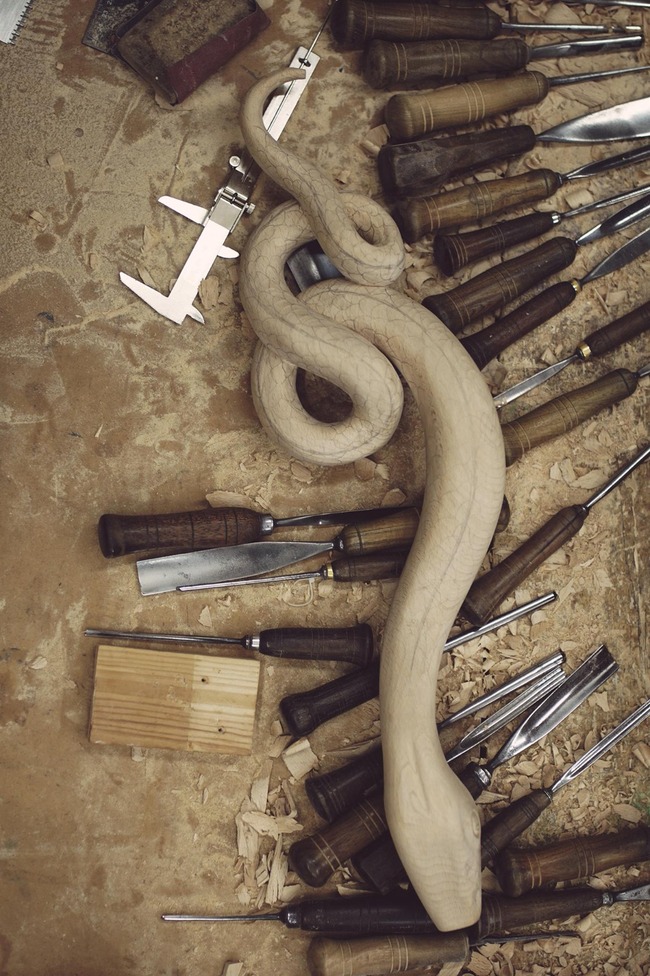 A wooden serpent is set on a production site, surrounded by woodworking tools.
