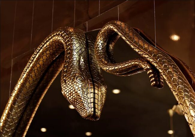 Detailed look on a exotic mirror frame, resembling a serpent, in golden hues.