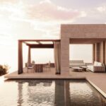 A vacation house by a pool, with two outdoor spaces. One of them has a dining table and four chairs surrounding it and the other space has rwo sofas and a golden center table.