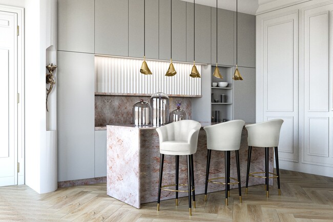 A kitchen in neutral colors, with grey compartiments, a light pink marble island, with three white upholstery counter stools and multiple golden pendant lights.
