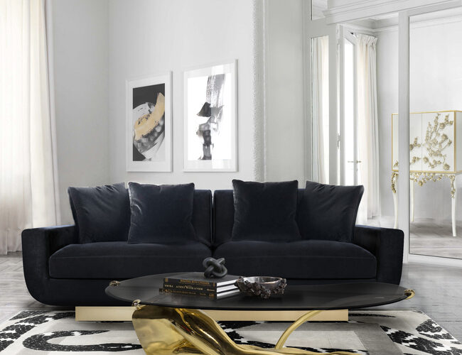 A modern and luxurious living room, in neutral colors. In the center of the room there is a black sofa, combining with the elegant center table, that serves a statement piece as it resembles the legs of a woman. In the background, there are frames with visual art.